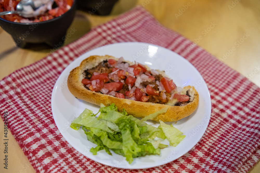 Mexican mollete and lettuce on a plate above white and red checkered napkin Mexican mollete and lettuce on a plate above white and red checkered napkin