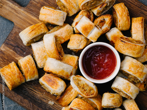 Sausage rolls on wooden board with tomato sauce