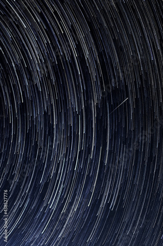 Stellar trails  the rotation of bright stars at night around the Polar Star against a blue sky and a meteor