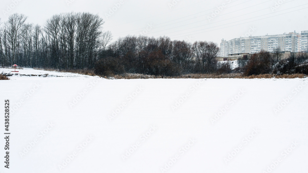 Winter urban Russian landscape, high-rise buildings, trees and a frozen pond covered with snow Winter urban Russian landscape, high-rise buildings, trees and a frozen pond covered with snow