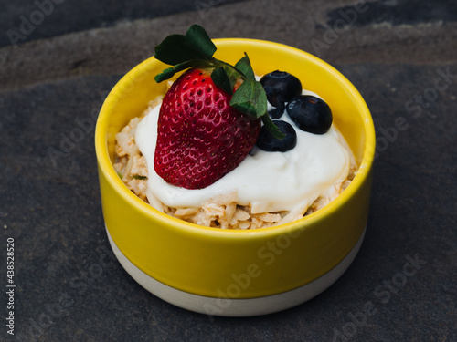 Bircher Muesli in a yellow ceramic bowl with yogurt and berries on top close up