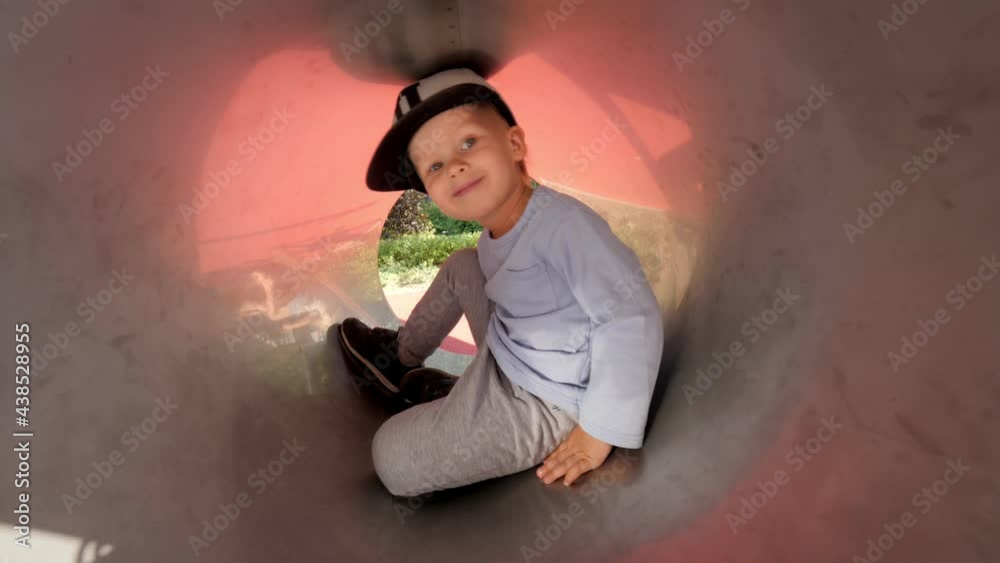 Cute male kid hiding in pipe slide attraction at amusement park enjoying outdoor summer activity Cute male kid hiding in pipe slide attraction at amusement park enjoying outdoor summer activity