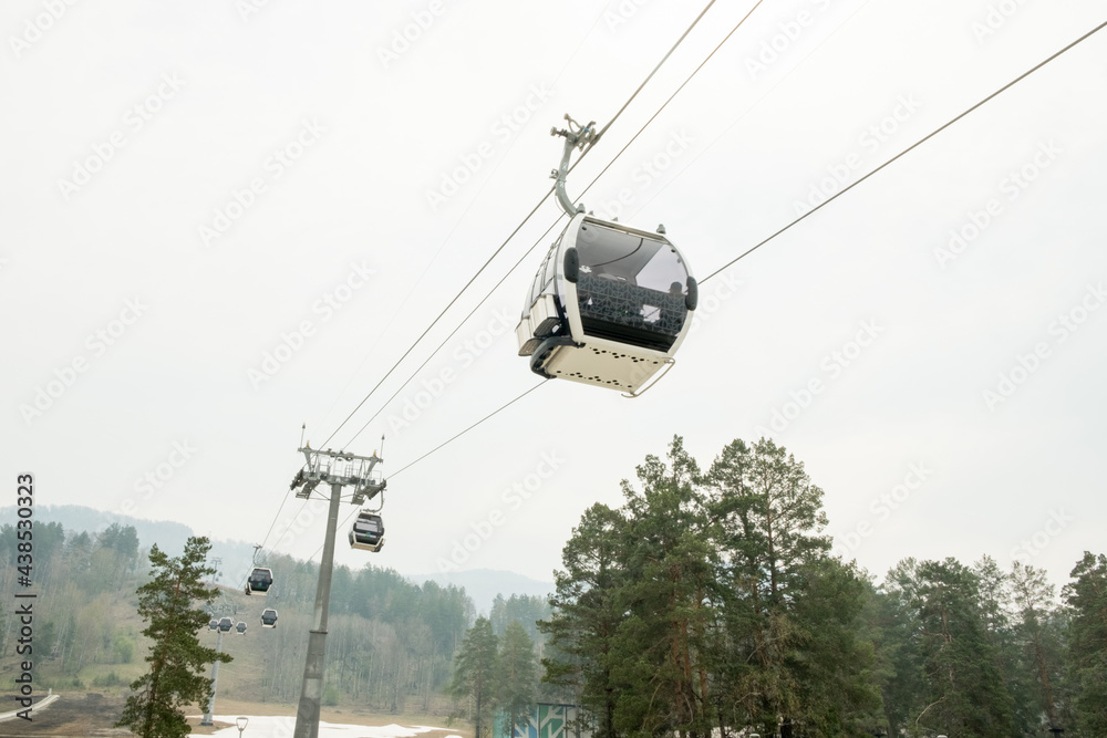 Lift cabins in a mountain ski resort. Ski lift ropeway on hilghland mountain winter resort on cloudy day. Ski chairlift cable way with people. Scenic panoramic wide view of downhill slopes.