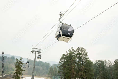 Lift cabins in a mountain ski resort. Ski lift ropeway on hilghland mountain winter resort on cloudy day. Ski chairlift cable way with people. Scenic panoramic wide view of downhill slopes.