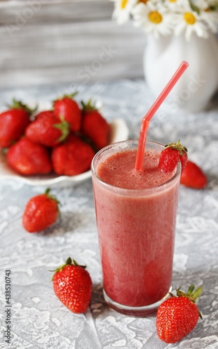 strawberry smoothie in a clear glass with a straw. Next to fresh strawberries. Useful dietary and organic food. For vegan and raw food nutrition. Light background. Soft focus.