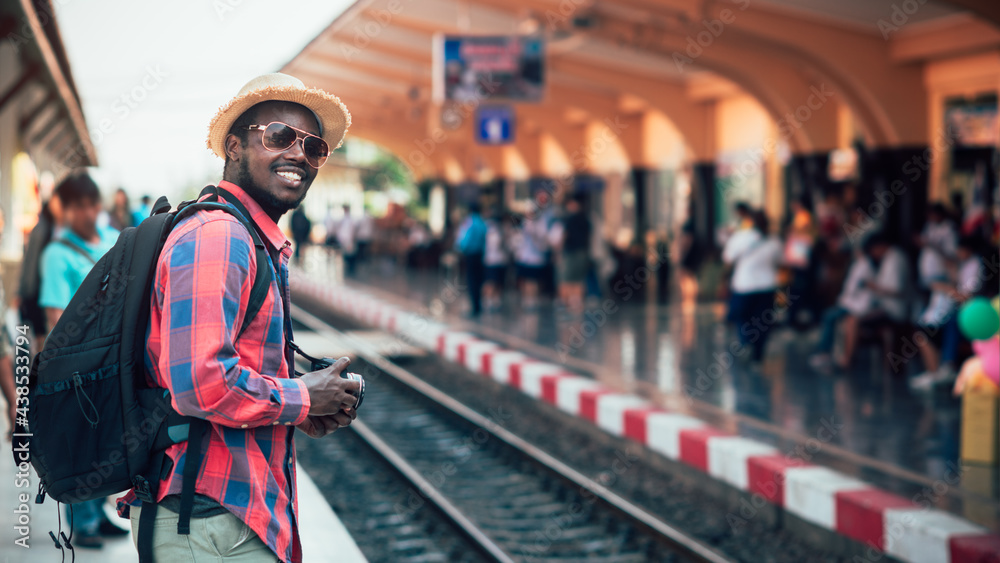 African male traveler with hat and backpack  waiting for the train on railway station.Adventure travel concept