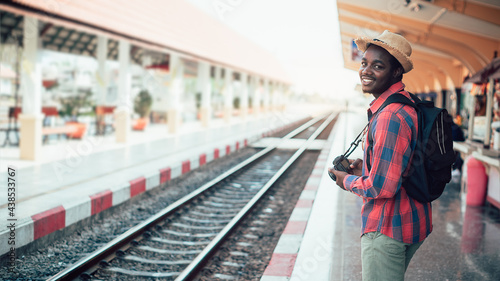 African male traveler with hat and backpack waiting for the train on railway station.Adventure travel concept