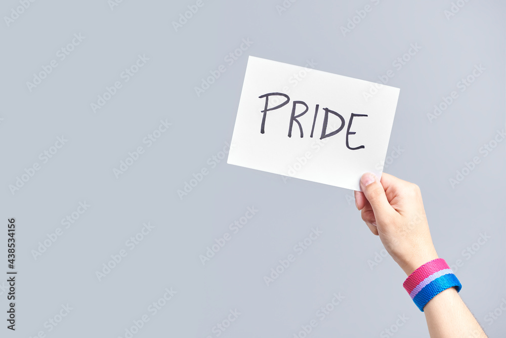Hand with a bisexual flag bracelet holding a paper with a message: pride Hand with a bisexual flag bracelet holding a paper with a message: pride