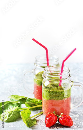 Two-layered smoothies made of strawberries and spinach in a trendy jar with a handle. Next to fresh strawberries and juicy spinach leaves. organic food. For vegan and raw food nutrition. 