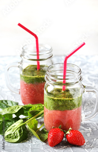 Two-layered smoothies made of strawberries and spinach in a trendy jar with a handle. Next to fresh strawberries and juicy spinach leaves. organic food. For vegan and raw food nutrition. © shabbydecor