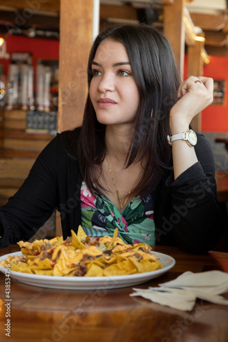 beautiful woman smiling with long hair  enjoying a plate of nachos  at a restaurant table  food and modern lifestyle