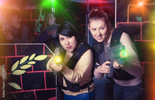 two emotional female laser tag players having fun in multinational team on laser tag arena