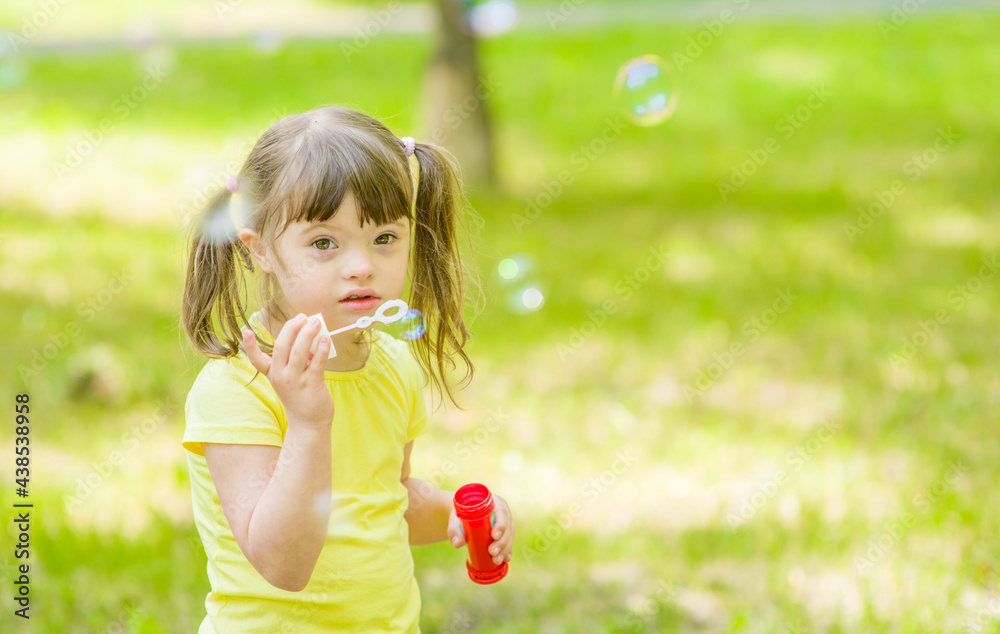 Little girl with syndrome down blows bubbles in a summer park Little girl with syndrome down blows bubbles in a summer park