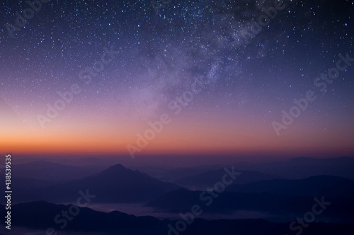 Milky way is visible in the dark night sky. Beautiful starry background with galaxy nebula and beautiful view of foggy landscape on top of mountain at the morning.