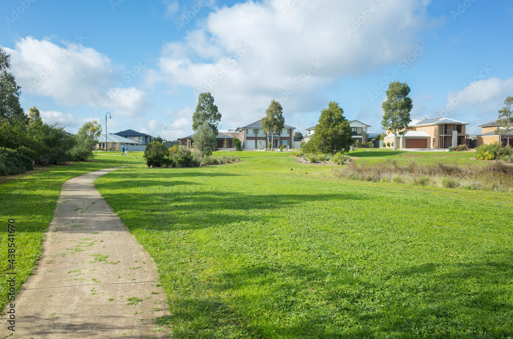 A nature reserve with a concrete footpath with some modern suburban houses in the distance. Concept of nature environment in residential area and the view in a typical Australian neighbourhood.