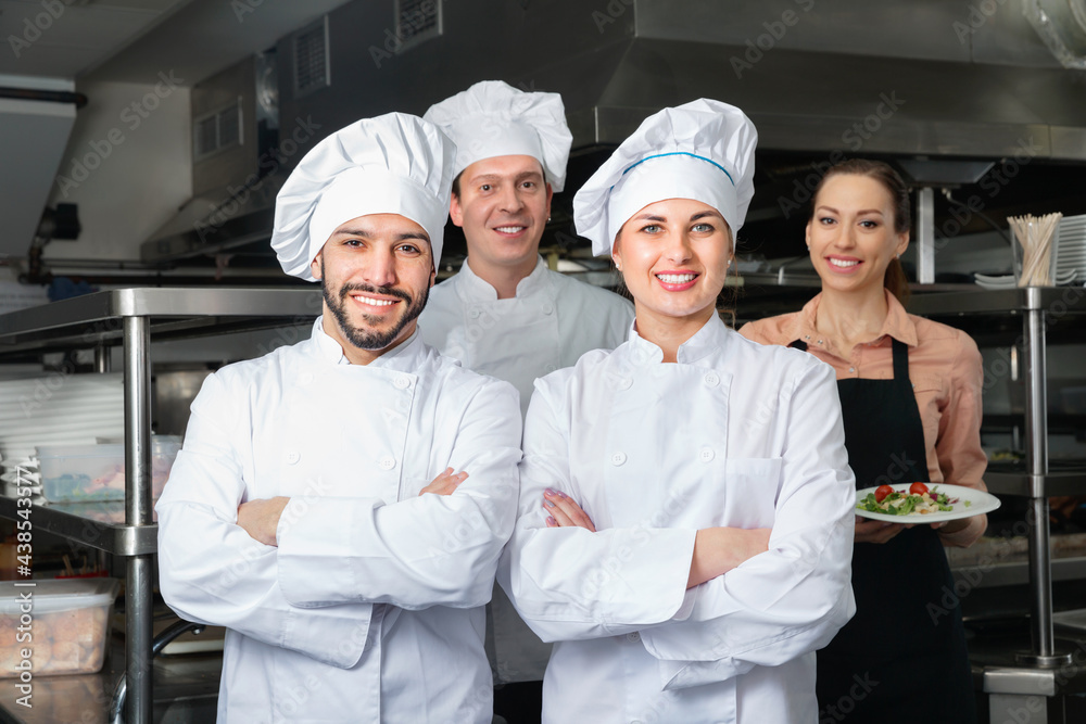 Portrait of two positive smiling confident cheerful chefs in kitchen with staff of restaurant
