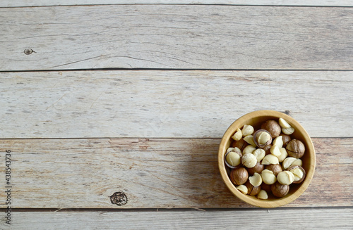 Top Views of Macadamia Nuts in a wooden bowl isolated on the wooden background, Healthy Food Concept.