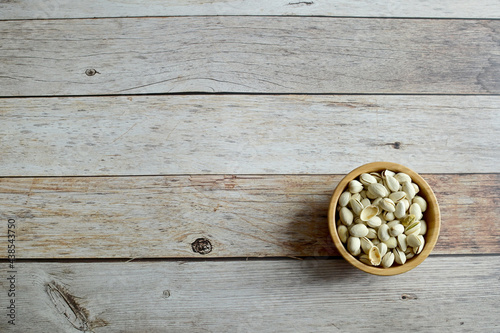Top Views of Pistachios in a wooden bowl isolated on the wooden background, Healthy Food Concept.