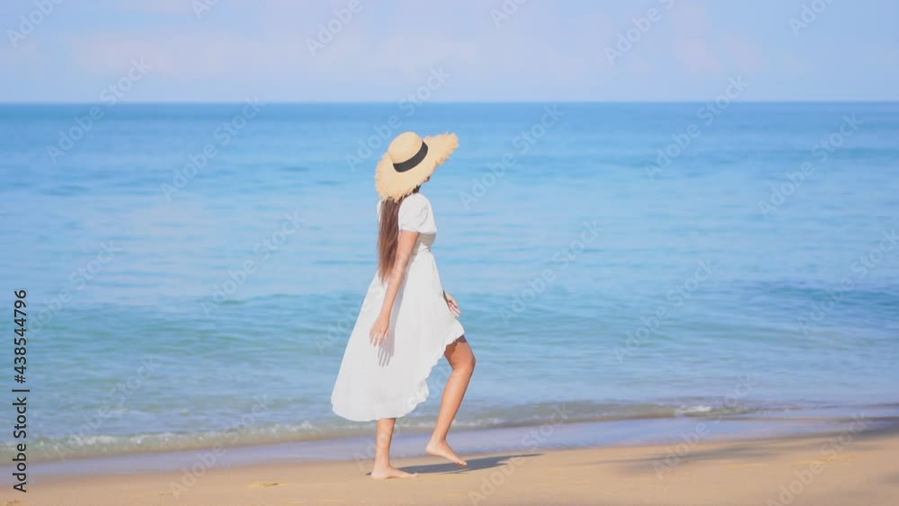 Barefoot woman with white dress walking on sandy beach with large straw hat. Slow-motion Barefoot woman with white dress walking on sandy beach with large straw hat. Slow-motion