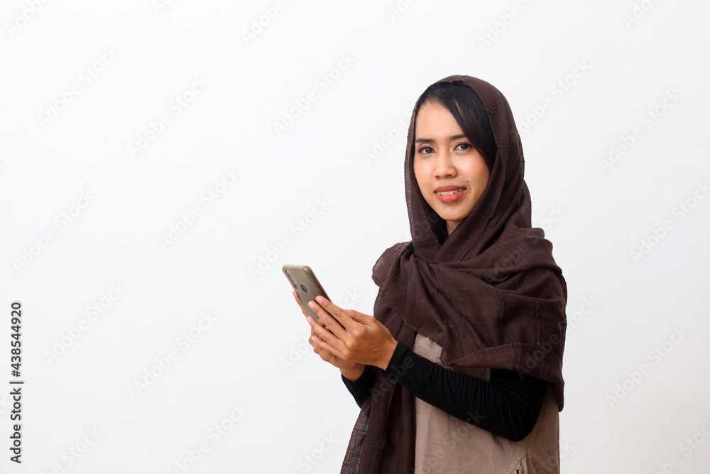 Portrait of happy asian muslim woman wearing a veil or hijab using a cell phone and smiling. Receiving good news, modern communication concept. Isolated on white background with copy space Portrait of happy asian muslim woman wearing a veil or hijab using a cell phone and smiling. Receiving good news, modern communication concept. Isolated on white background with copy space