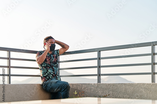 young latino man working and talking on the phone on the roof of the building