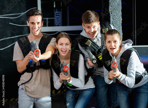 Happy glad positive smiling young people with laser pistols posing together on dark laser tag labyrinth