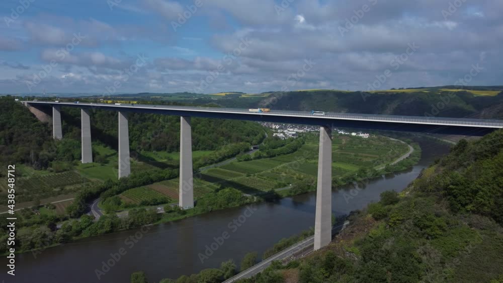 Aerial drone pan shot of crossing vehicles on Moselle Bridge during summer day in Germany. Beautiful landscape with green hills and river. Aerial drone pan shot of crossing vehicles on Moselle Bridge during summer day in Germany. Beautiful landscape with green hills and river.