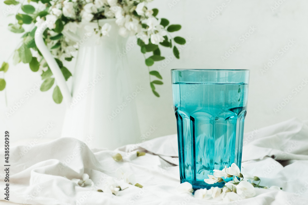 Obraz premium acacia flowers broth in blue glassware cup on cement background with lush flowering white acacia tree Branch , home self-treatment, useful properties of plants