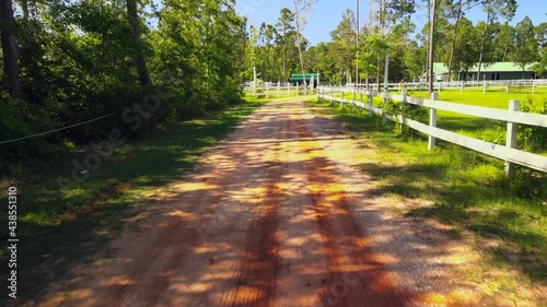 Flying along a quiant path along the woods revealing a picturesque horse ranch with pastures and white picket fences photo