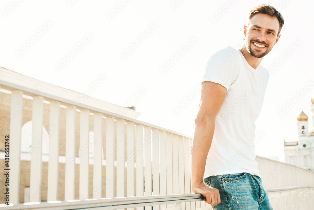 Portrait of handsome smiling hipster lambersexual model.Stylish man dressed in white T-shirt and jeans. Fashion male posing on the street background near fence at the beach in sunglasses Portrait of handsome smiling hipster lambersexual model.Stylish man dressed in white T-shirt and jeans. Fashion male posing on the street background near fence at the beach in sunglasses