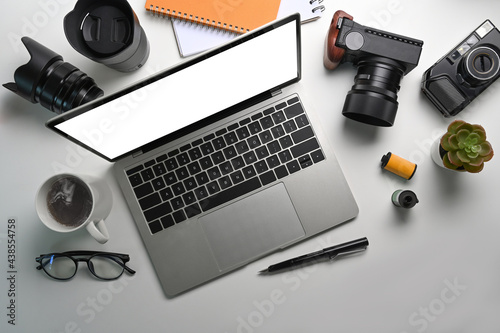 Above view of photographer workspace with laptop computer, camera, coffee cup and glasses on white table.