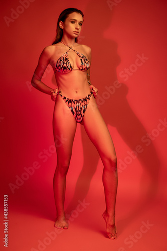 Young woman in string bikini swimsuit posing on crimson background