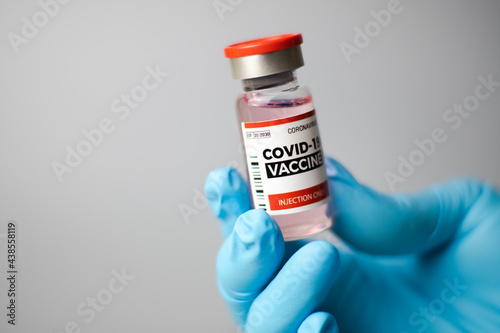 A doctor wearing blue gloves picks up a bottle of COVID-19 vaccine. On a gray-white background, Prevent and cure corona virus. close up