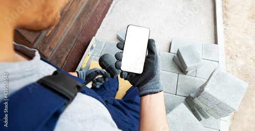 Fototapeta bricklayer holding the phone with blank screen in hand on gloves
