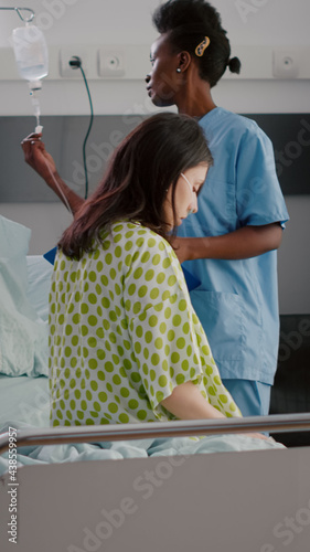 Afro american asisstant monitoring hospitalized sick woman with respiratory illness recovering after medical surgery. African nurse working in hospital ward explaining treatment to patient photo