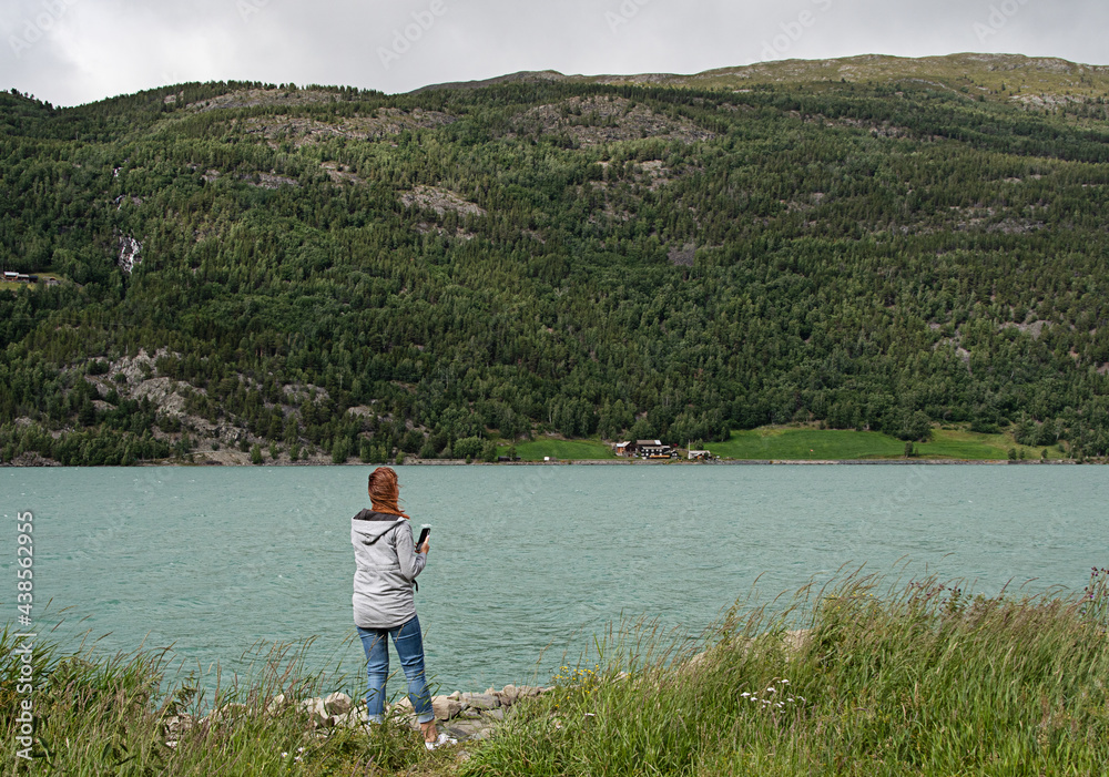 Woman photographs the turquoise lake. The color is caused by algae from melting snow in the mountain Woman photographs the turquoise lake. The color is caused by algae from melting snow in the mountain