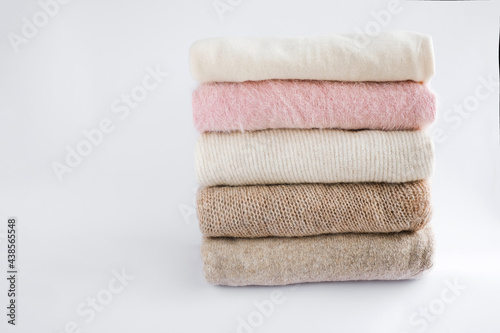 cozy milky beige and white natural wool sweaters, folded on a white background close-up. clothes made of merino wool, alpaca, natural eco-fabrics. the concept of conscious consumption. flat lay