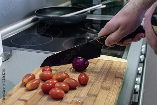 Man cuts red onion in kitchen at home against plate photo