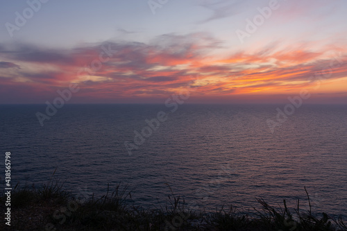 Pink sunset on the sea. Bright juicy landscape with low cumulus clouds on the horizon. Purple  lilac and pink shades of the evening sky. Waves on the surface of the sea  a stone shore. Beautiful surf