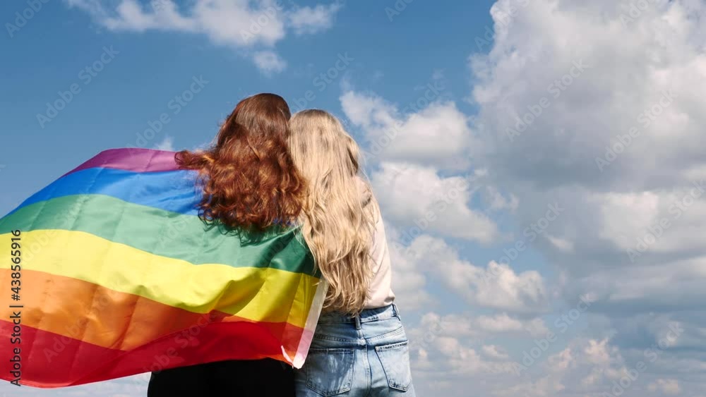Two women girlfriends holding a symbol of LGBT flag on the background