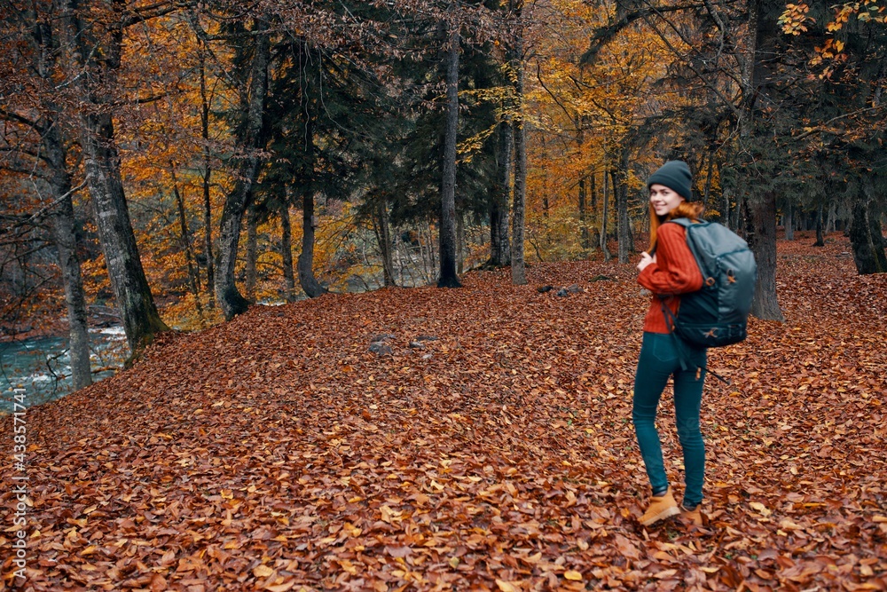 woman with backpack hiking travel in autumn park tall trees river fallen leaves