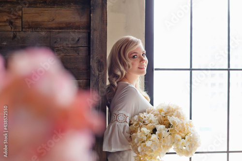 Morning of the bride. A gorgeous bride, a beautiful woman with long hair in a white robe by the window. The bride before the wedding. Natural beauty and professional makeup.