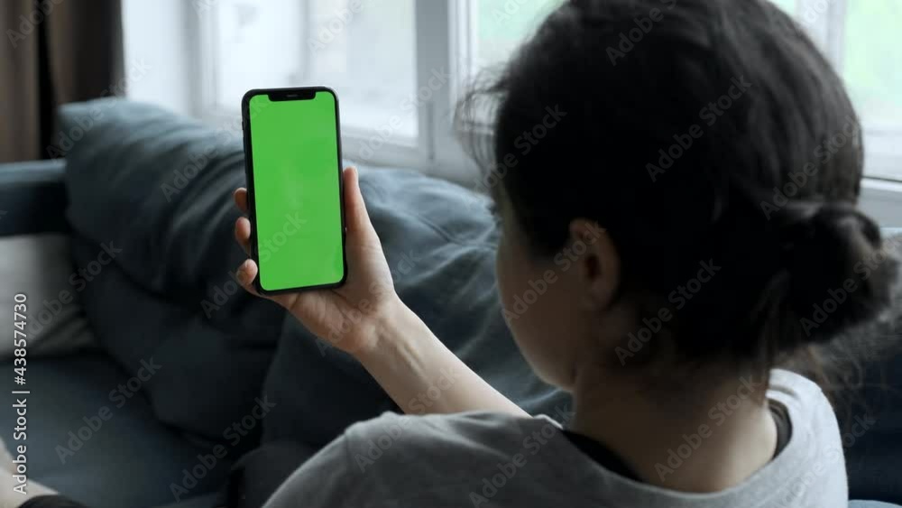 A Woman's Hand Holds A Smartphone With A Green Screen For Chromakey, Watches Social Networks, Movies, Videos, Lies on The Sofa in A Cozy Room A Woman's Hand Holds A Smartphone With A Green Screen For Chromakey, Watches Social Networks, Movies, Videos, Lies on The Sofa in A Cozy Room