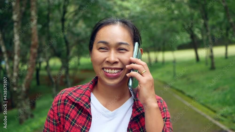 A cheerful female tourist talks on her smartphone with a smiling face and relaxes in a nature park. concept of technology and happiness. A cheerful female tourist talks on her smartphone with a smiling face and relaxes in a nature park. concept of technology and happiness.