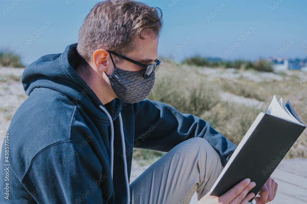 young man with medical mask reading a book on the street in the new normal