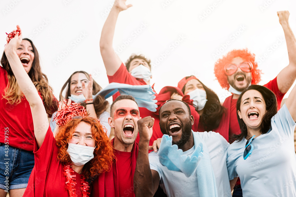 Group of multiracial supporters wearing protective face mask screaming while supporting their team in the stadium - New normal for live sports concept - Focus on black man face