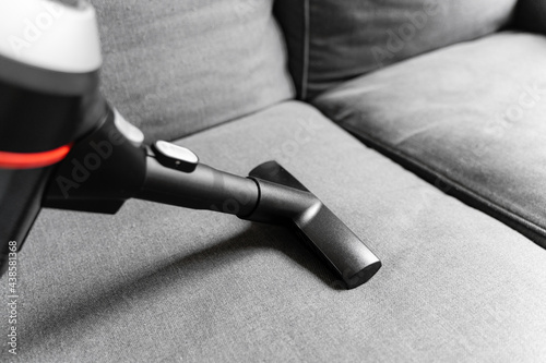 Cleaning grey sofa with wireless vacuum cleaner. Handheld cordless cleaner. Household appliance. Housework modern equipment