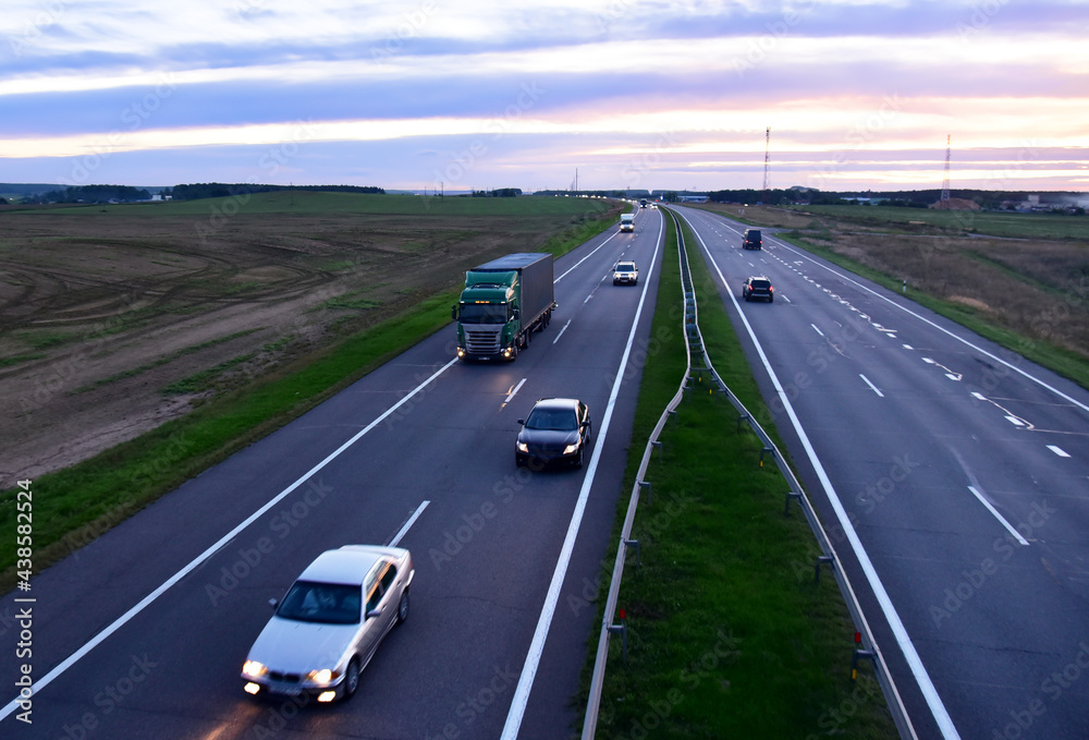 Car traffic on the road. Truck with semi-trailer driving along highway on sunset background. Goods Delivery by roads. Services and Transport logistics. Car traffic on the road. Truck with semi-trailer driving along highway on sunset background. Goods Delivery by roads. Services and Transport logistics.