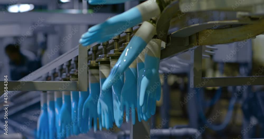Silicone medical gloves on plastic molds rotate on a conveyor belt