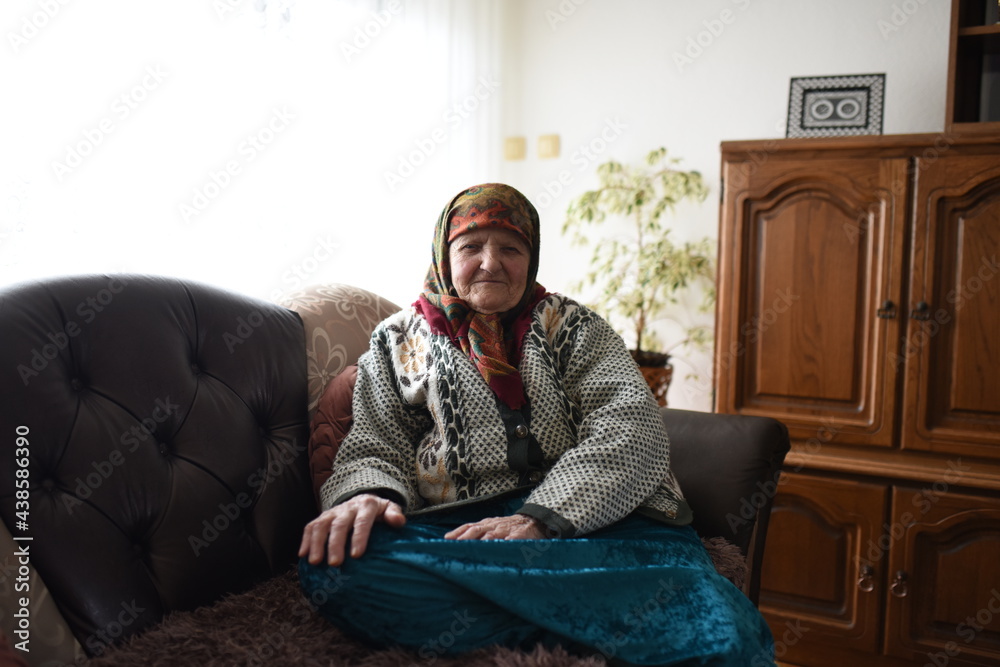 Fototapeta premium a very old woman in traditional Muslim clothes sitting in the house next to the window